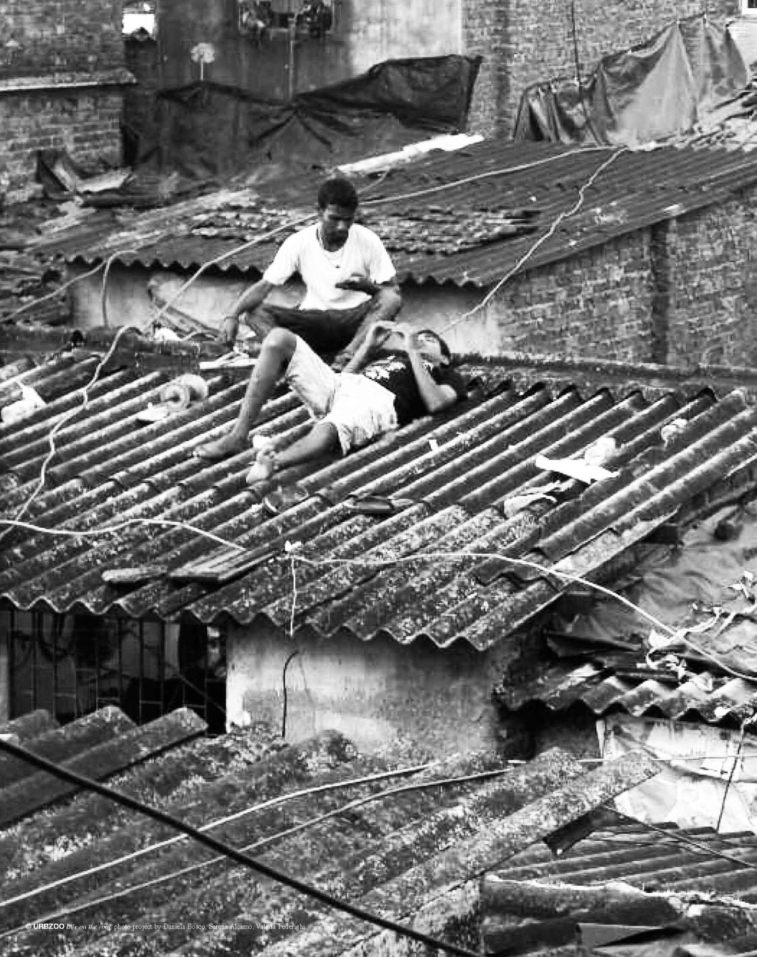 Two figures resting on corrugated rooftops at dusk
